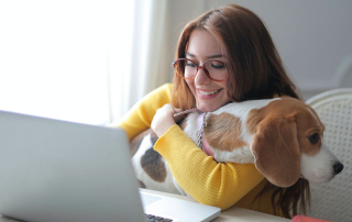 FEMME DEVANT UN ORDINATEUR TENANT SON CHIEN DANT LES BRAS