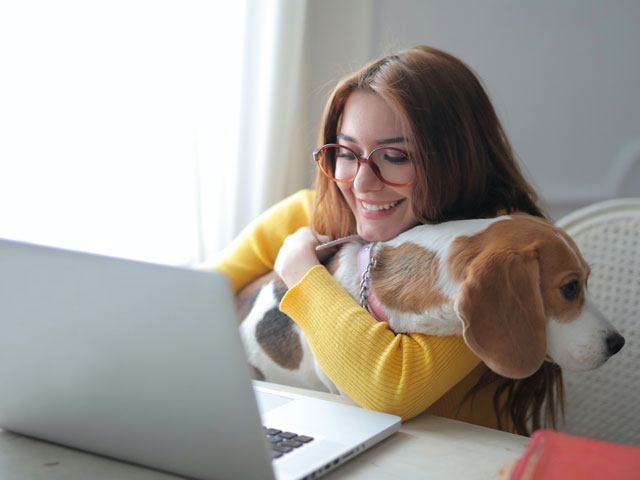 FEMME DEVANT UN ORDINATEUR TENANT SON CHIEN DANT LES BRAS