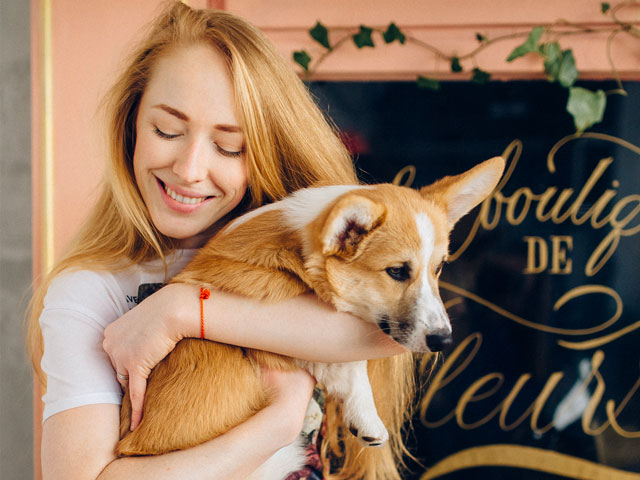 FEMME PORTANT UN CHIEN DE RACE CORGI DANS SES BRAS